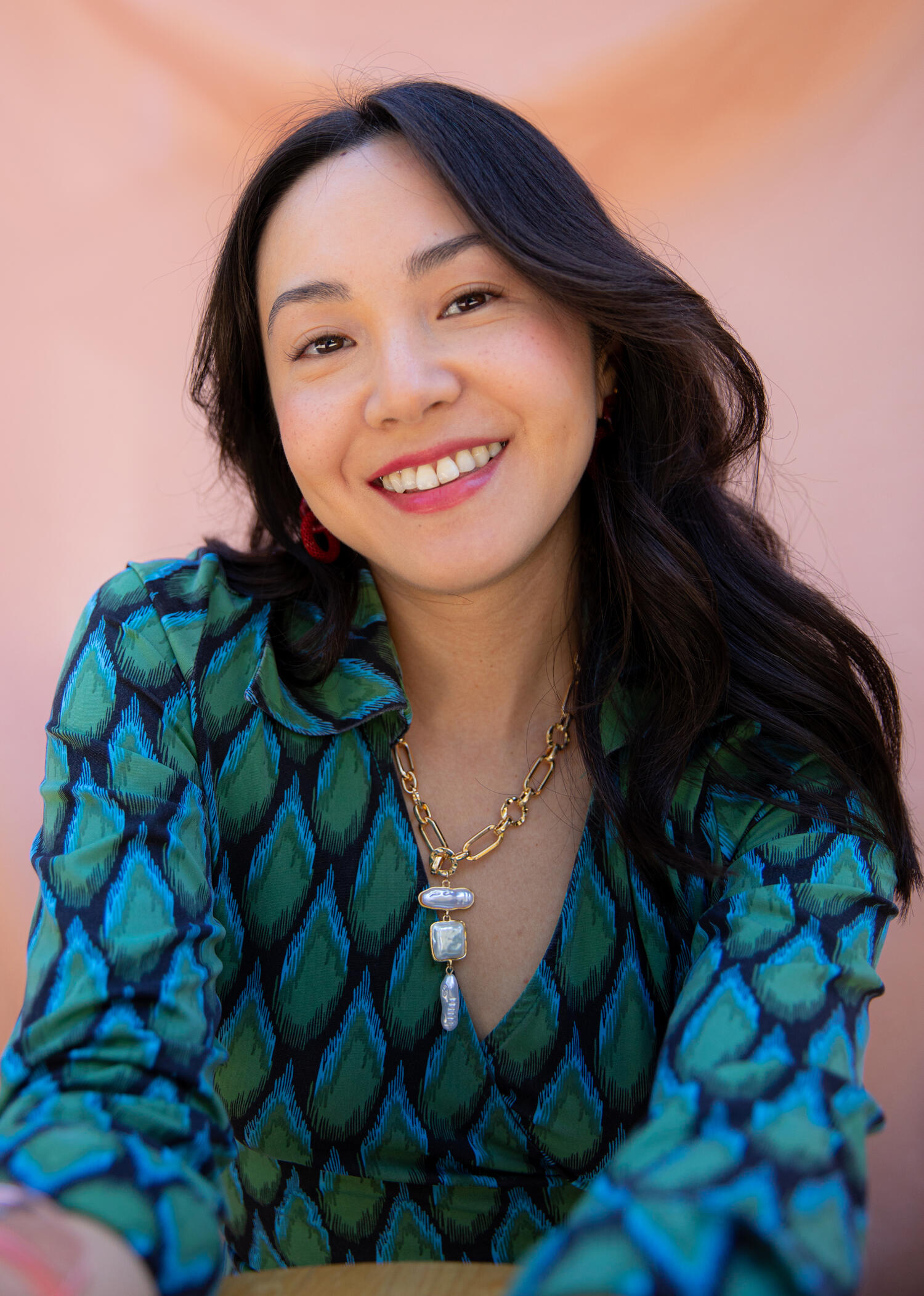 portrait of the author looking into the distance. she is sitting and wearing a green wrap dress, gold chain, and red earrings